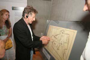 Roman Polanski stands in front of map of Krakow Ghetto in the Holocaust History Museum and describes his escape from that Ghetto