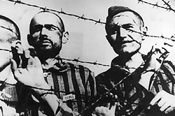 Auschwitz-Birkenau, Lengyelország, táborlakók néznek ki a tábor szöges kerítése mögül